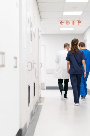 Rear view of doctor and nurse walking in hallway while discussing a case. Group of doctor and nurses in uniform examining medical report of patient while walking on hospital corridor. Medical staff working at private clinic, copy space.