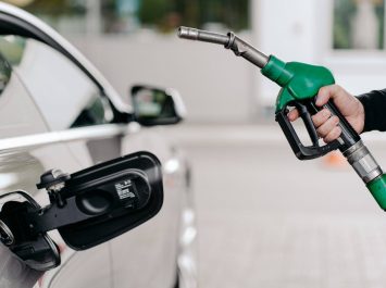 Cropped shot of mans hand pumping gasoline fuel in car at gas station. Auto being filled with petrol. Unrecognizable man holds fuel nozzel.