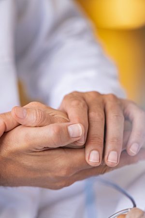 Close up of doctor hands holding senior patient's hands and comforting her. Close up of general practitioner holding senior woman hand giving assurance and comfort. Doctor comforting patient at consulting room. Help, support and caring concept.
